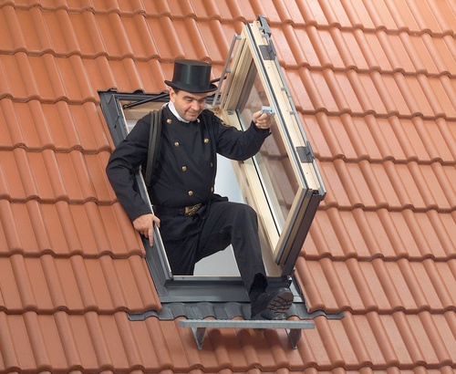 Ein Mann im Zylinder und Anzug steht auf dem Dach eines Hauses